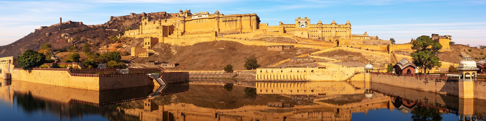 Un complejo histórico de fortaleza y palacio con una extensa masa de agua en primer plano que refleja las estructuras.