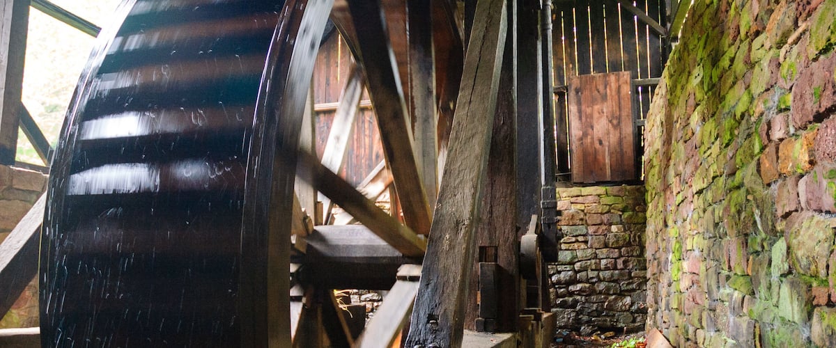 A large water wheel in a rustic setting with stone walls and wooden beams.