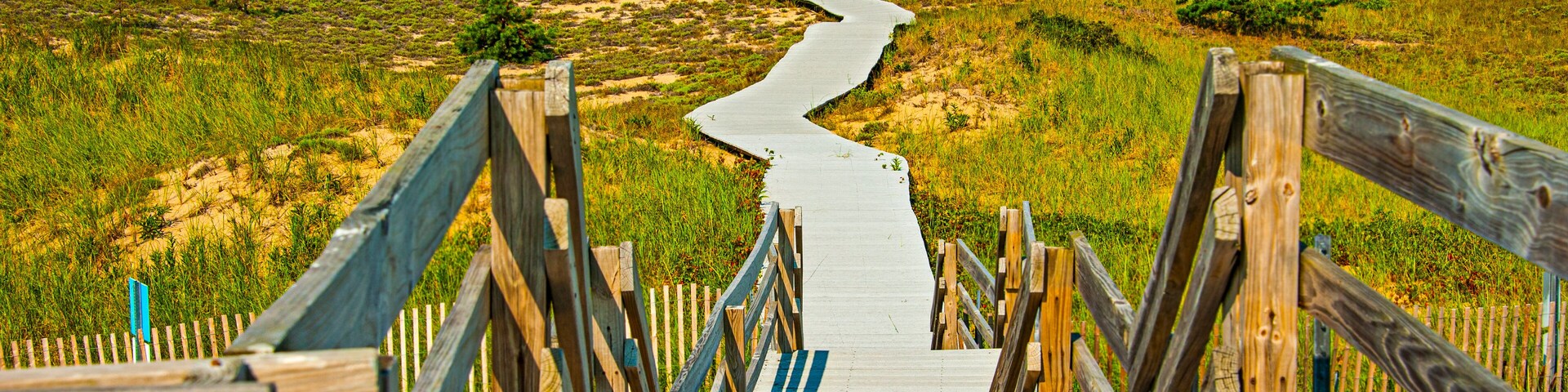 A wooden boardwalk leading up a sandy hill with a blue and white striped path.