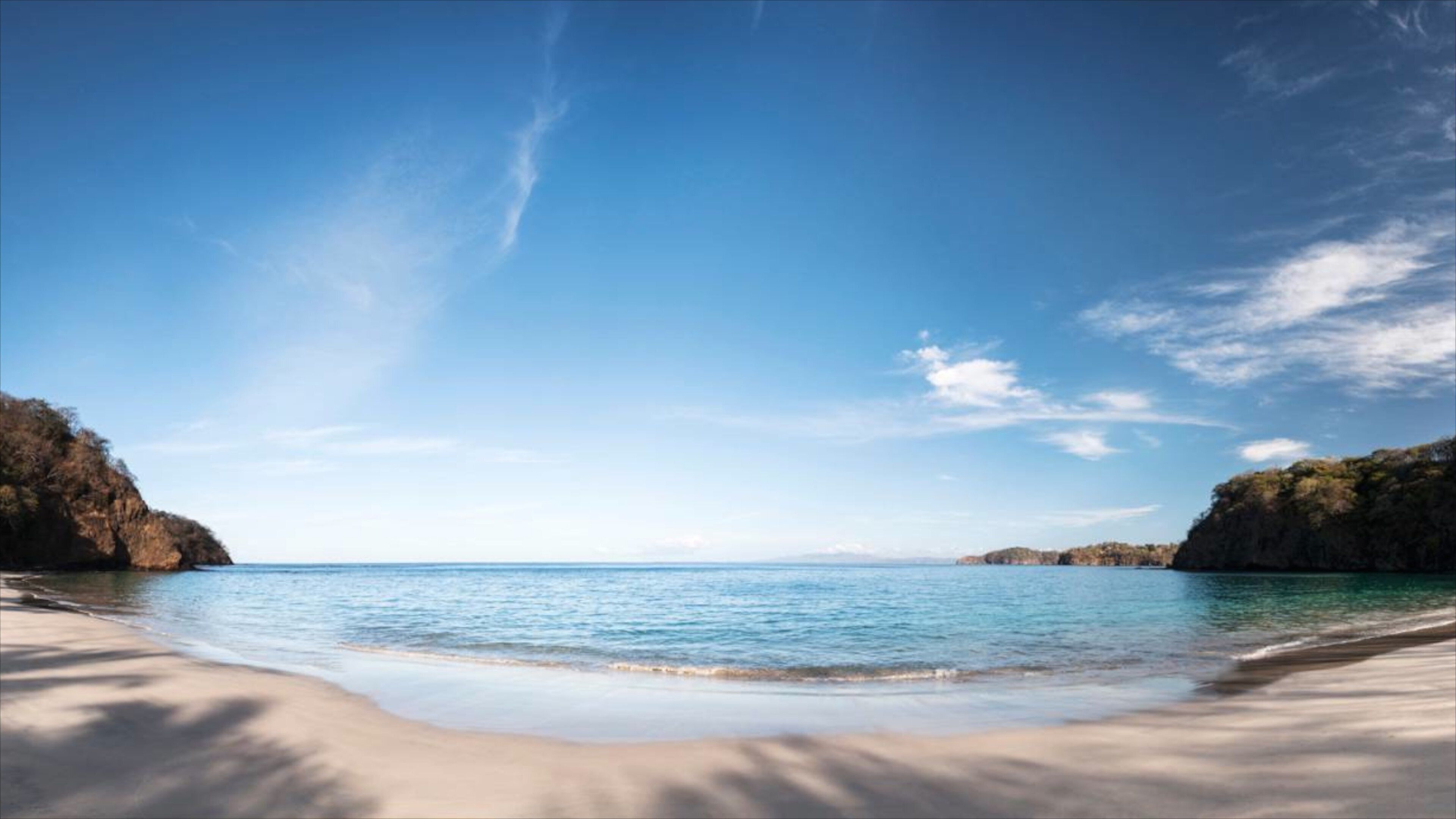 A beach with clear blue water, sandy shore, and rocky cliffs.