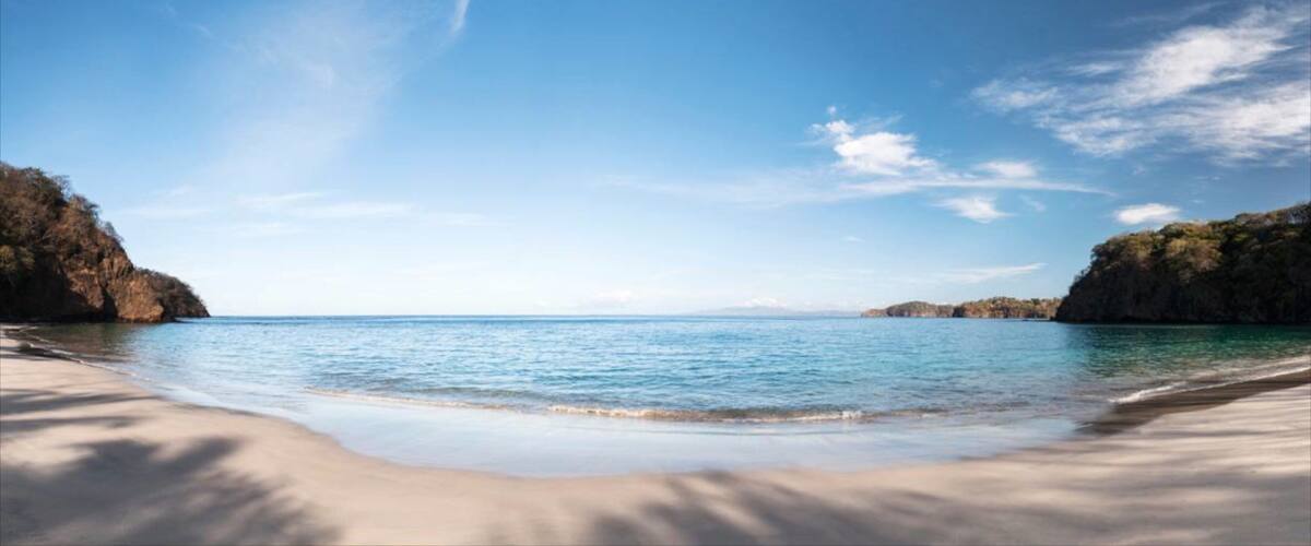 A beach with clear blue water, sandy shore, and rocky cliffs.