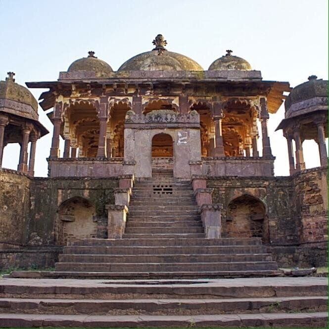 A historical building with multiple domes, a central archway, and a staircase leading up to it.