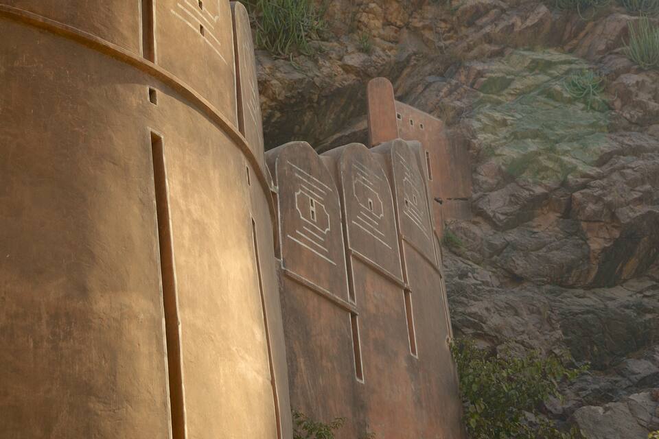 A large, cylindrical stone structure with carved symbols, set against a rocky hillside.