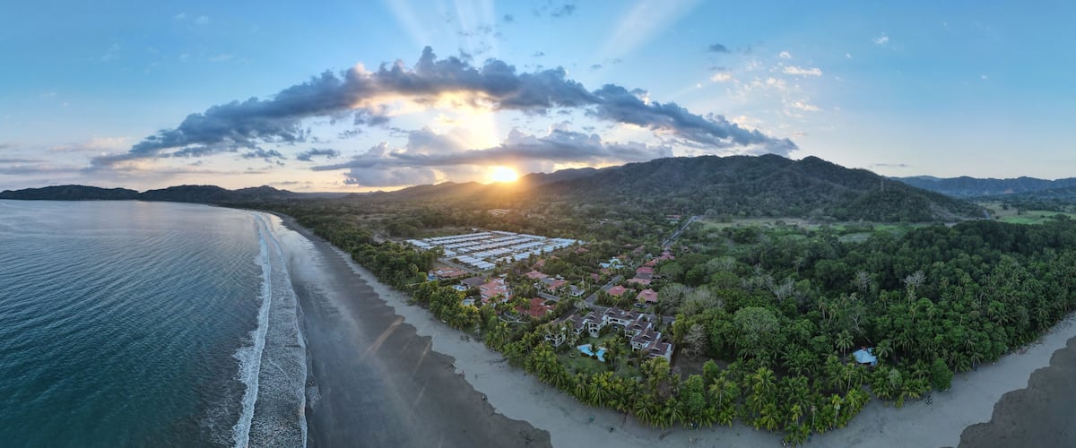 A coastal landscape with a beach, a residential area with houses, and a forested hill.