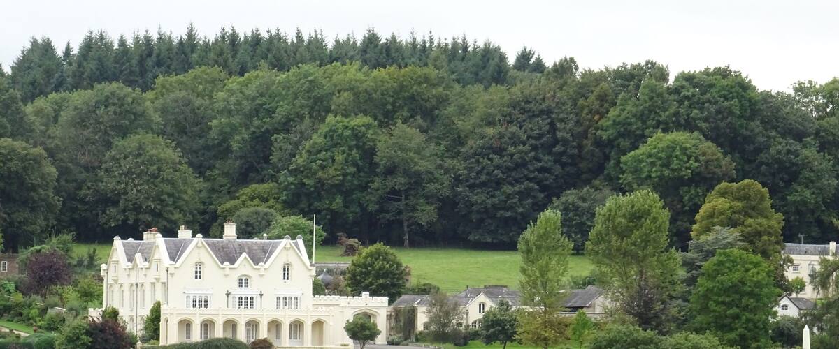 A large white manor house surrounded by lush green fields and trees.
