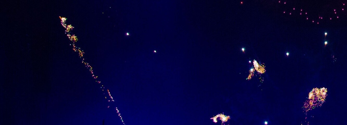 Cielo nocturno con fuegos artificiales y siluetas de personas sosteniendo un paraguas.