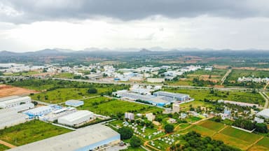 Zona industrial com edifícios grandes, campos verdes e montanhas ao longe.