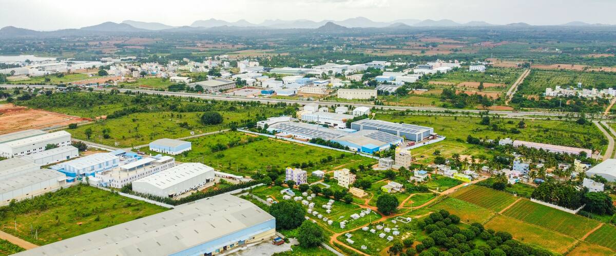 An industrial area with large buildings, green fields, and distant mountains.