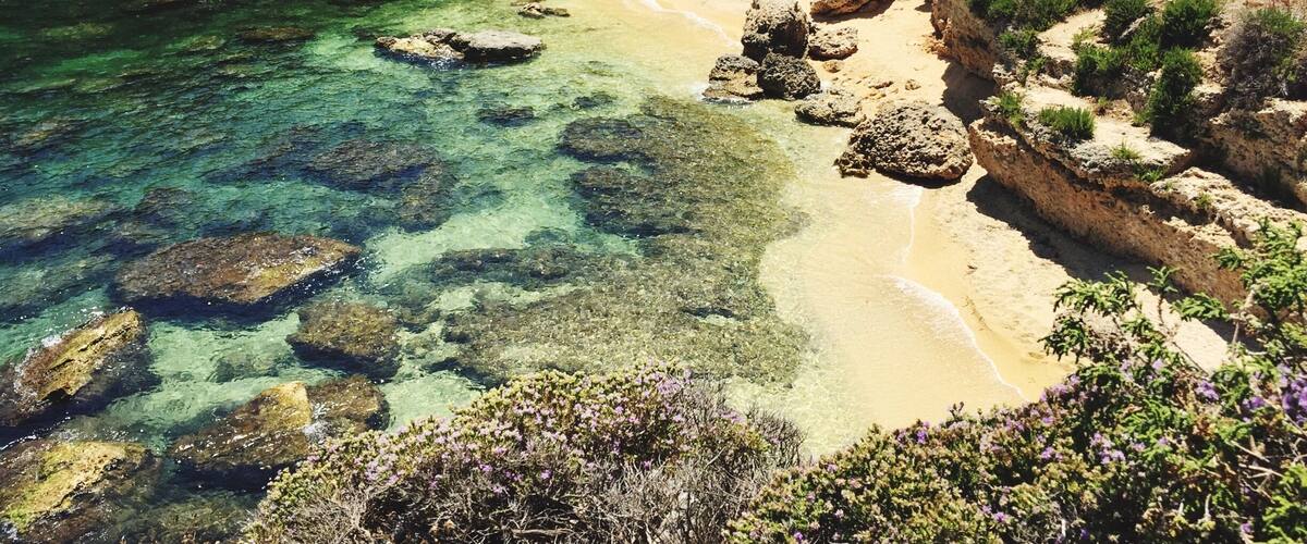 A coastal landscape with clear waters, sandy beach, and rocky formations.
