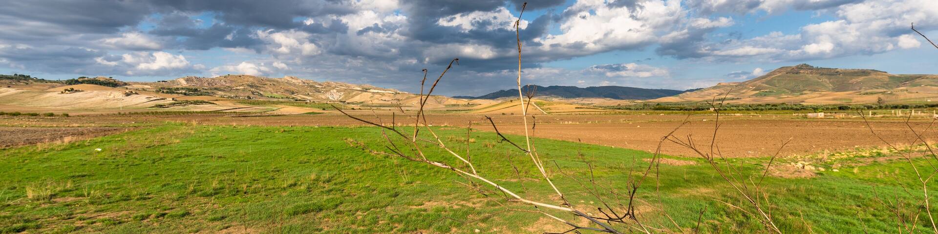 A landscape with green fields, a cloudy sky, and distant hills.