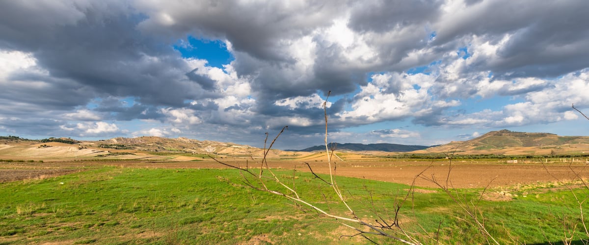 A landscape with green fields, a cloudy sky, and distant hills.