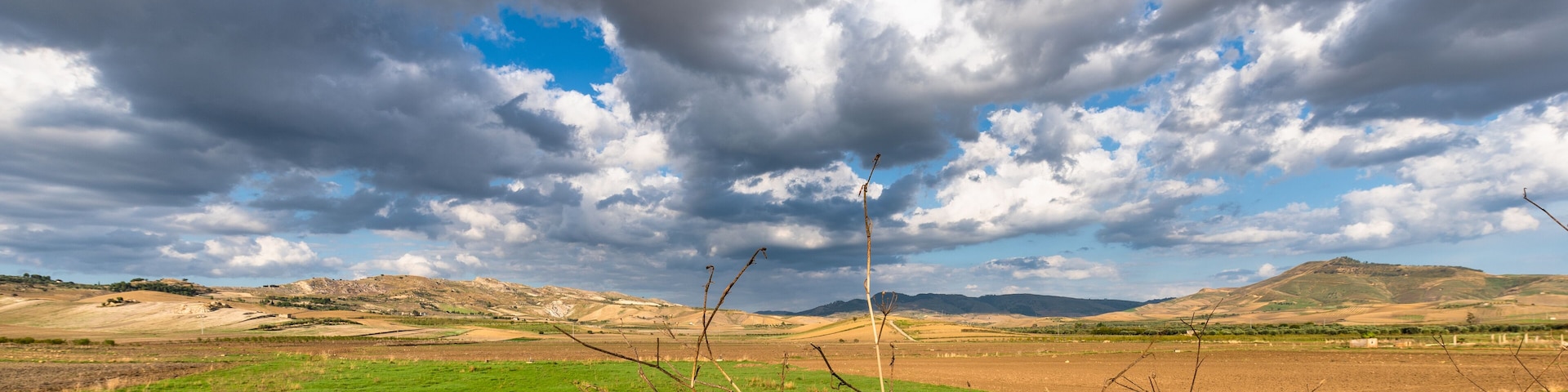 A landscape with green fields, a cloudy sky, and distant hills.