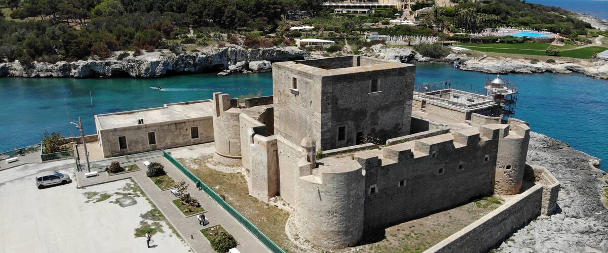 A coastal castle with a large tower, surrounded by a fortified wall and a parking area.