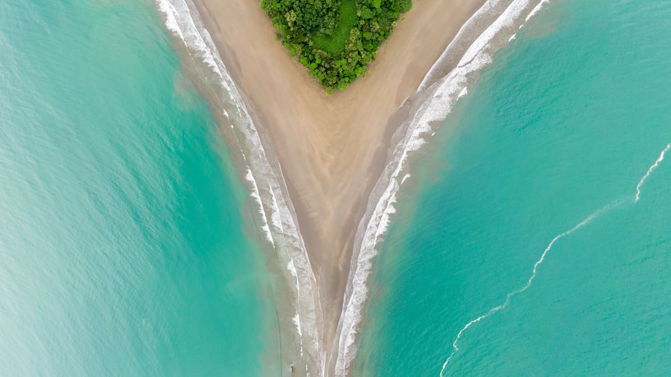 An aerial view of a beach with turquoise waters, a sandy shoreline, and a small green island.