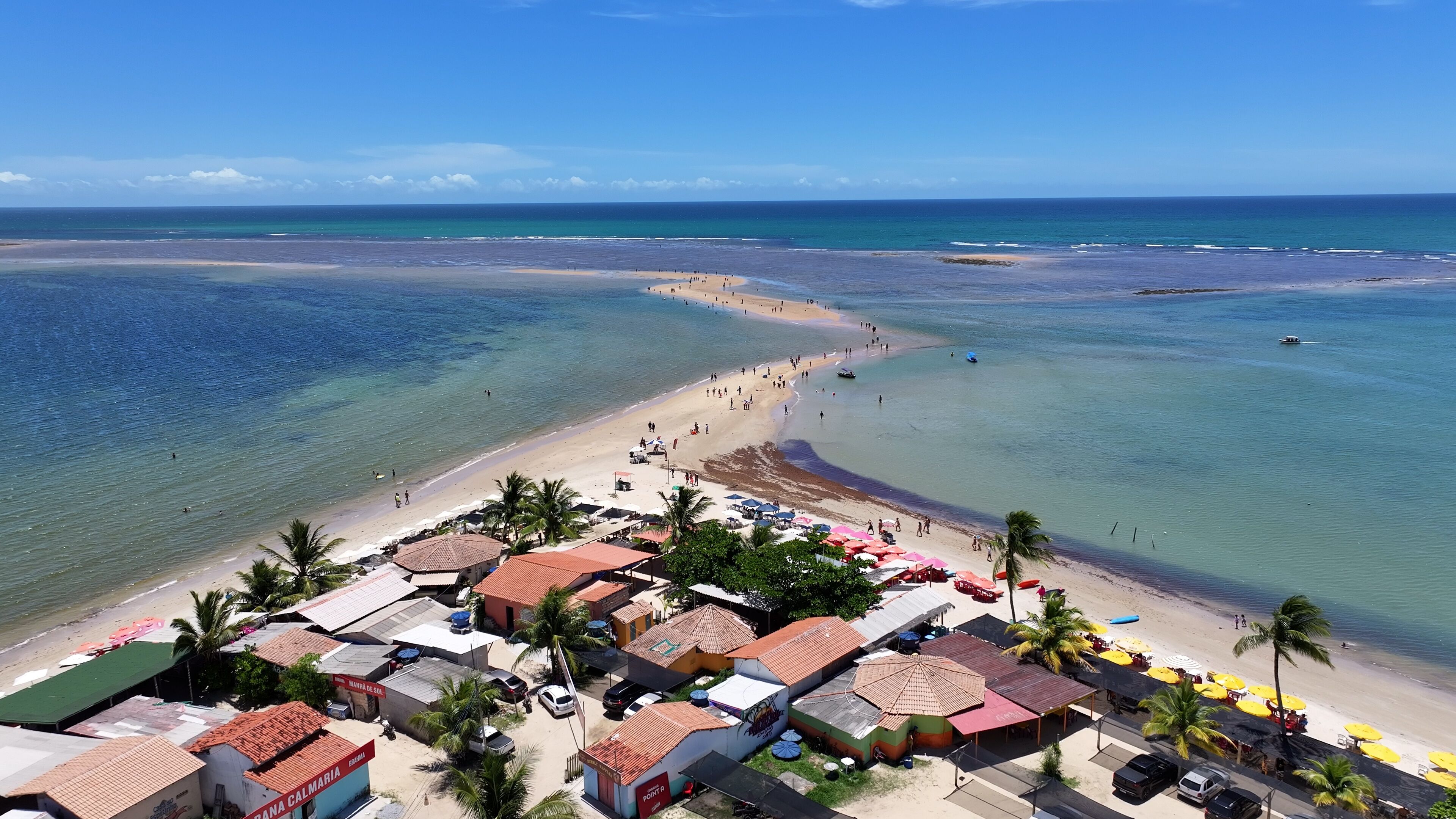 Uma praia com águas cristalinas, um areal e uma fileira de edifícios à beira-mar.