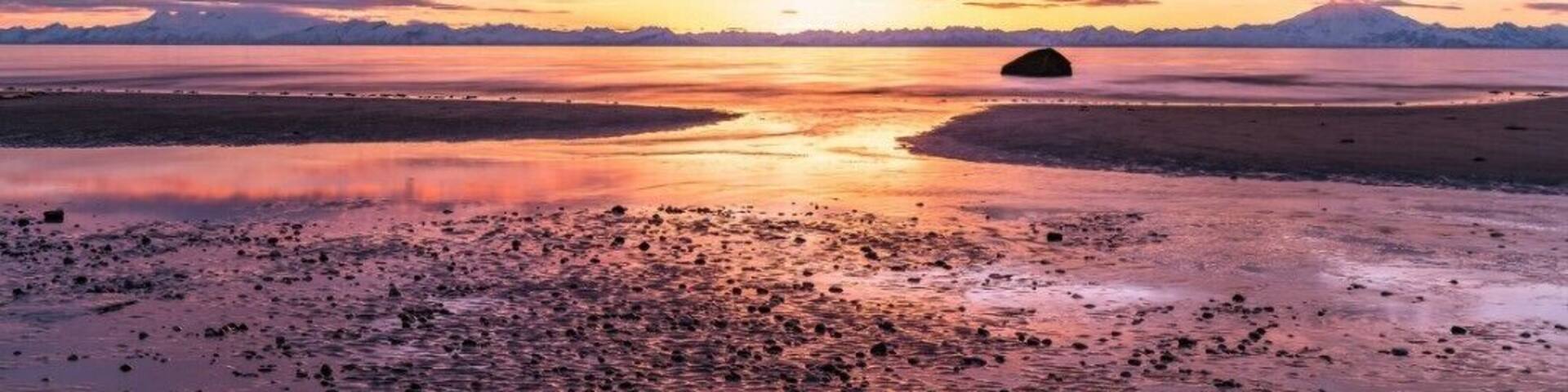 Un atardecer sobre un lago tranquilo con montañas al fondo.