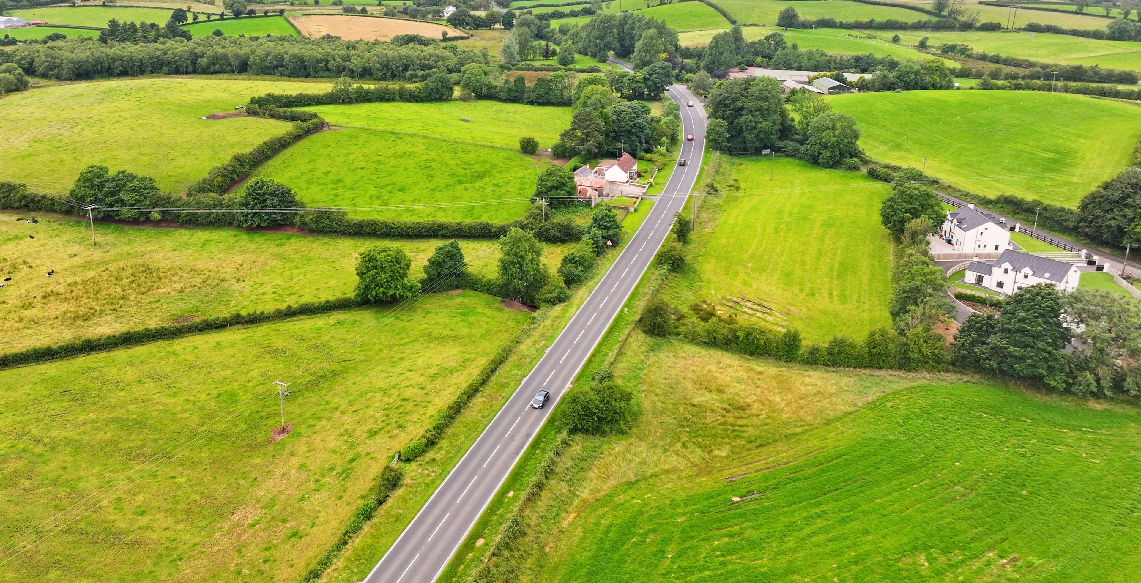 A rural landscape with a winding road, green fields, and scattered houses.