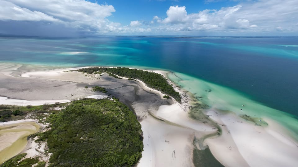 A coastal landscape with white sandy beaches, clear turquoise waters, and lush green vegetation.