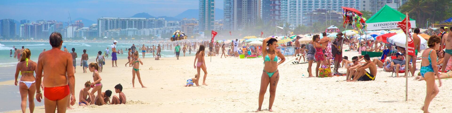 A crowded beach with people in bikinis and swim trunks, umbrellas, and tall buildings in the background.
