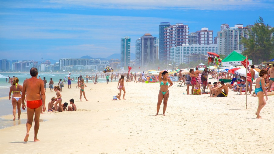 A crowded beach with people in bikinis and swim trunks, umbrellas, and tall buildings in the background.