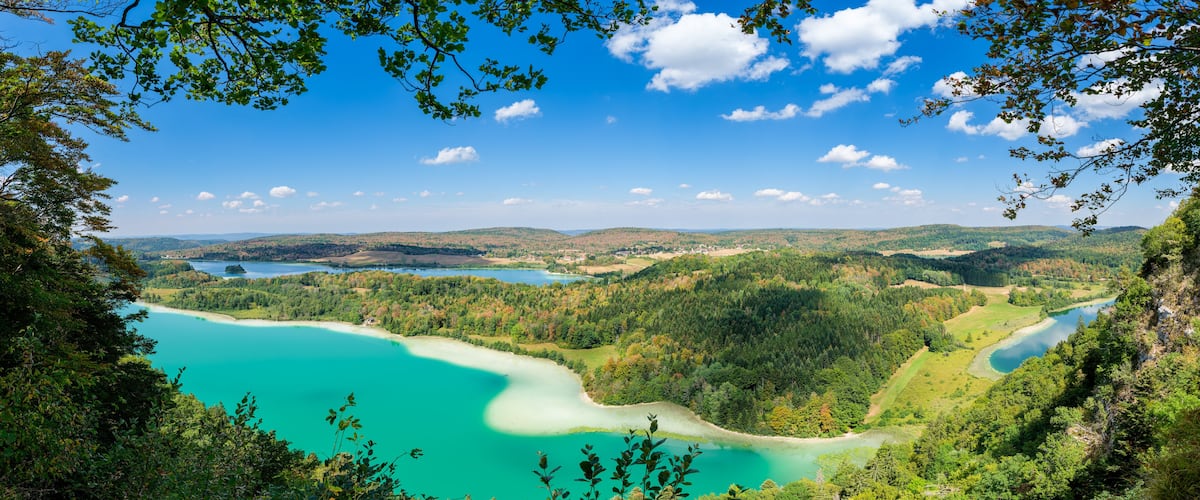 A turquoise lake surrounded by forested hills and a clear blue sky.