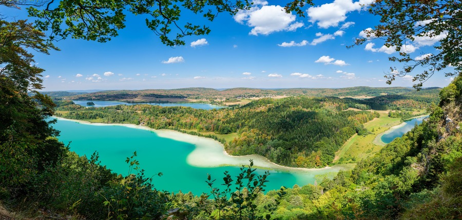 A turquoise lake surrounded by forested hills and a clear blue sky.