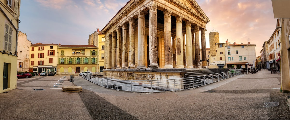 A classical building with columns, a fountain, and surrounding urban architecture.