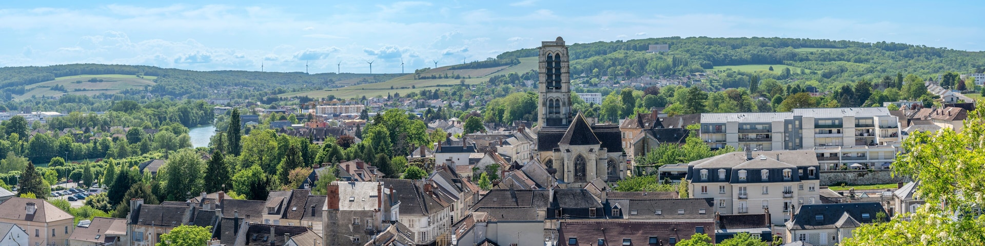 Eine Stadt mit einem markanten Kirchturm, einem Fluss und sanften Hügeln im Hintergrund.