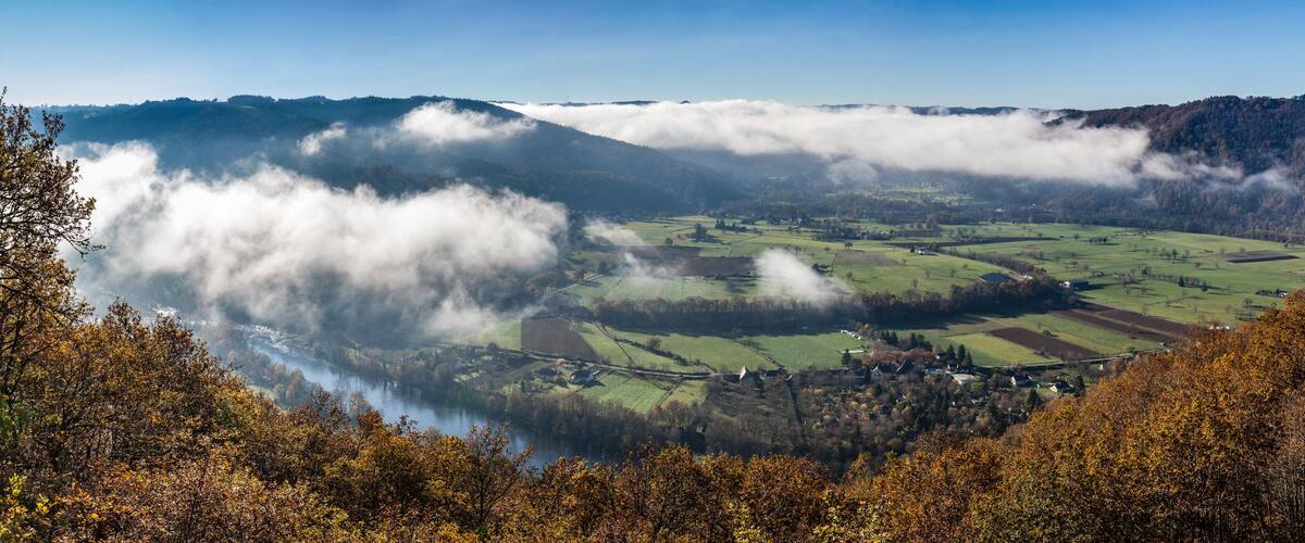 A valley with a river, fields, and a mountain range partially covered by clouds.