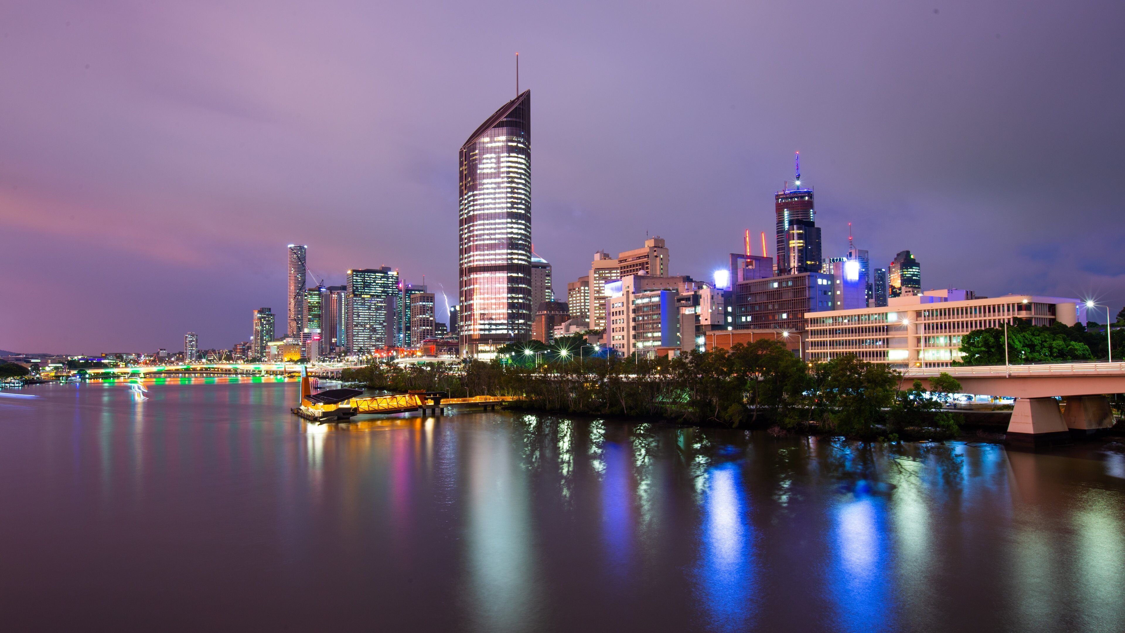 Un horizonte urbano nocturno con edificios iluminados y un río que refleja las luces.