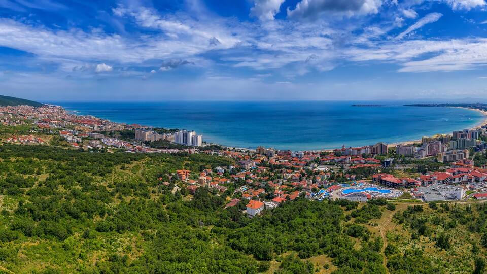 A coastal city with a beach, dense residential area, and a mountainous backdrop.
