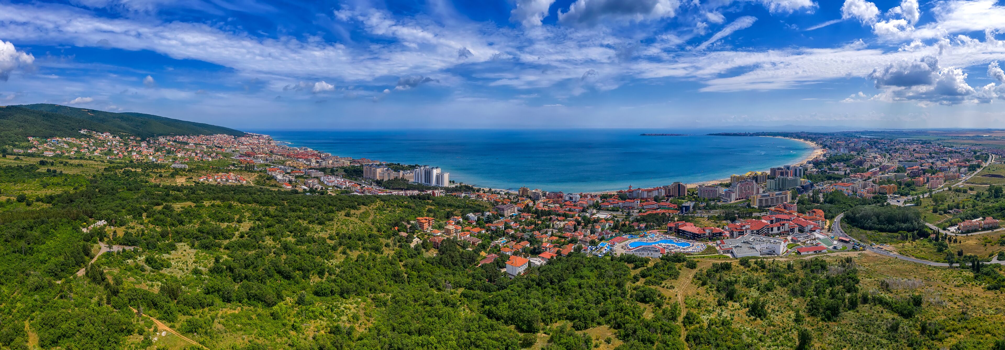 A coastal city with a beach, dense residential area, and a mountainous backdrop.