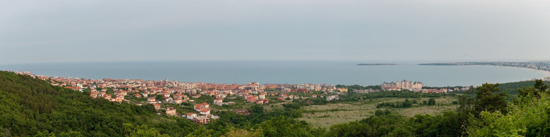 Un paisaje urbano costero con edificios apretados, una extensa masa de agua y un terreno montañoso en primer plano.