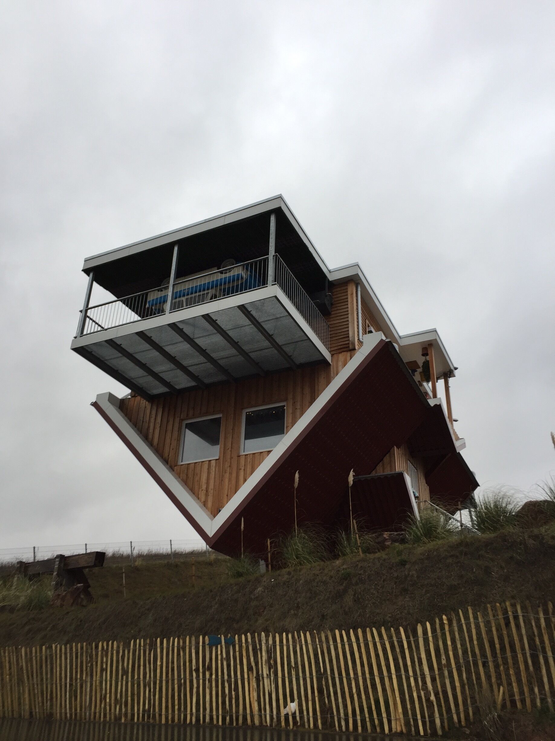 A modern, multi-level wooden house with a slanted roof and a balcony.