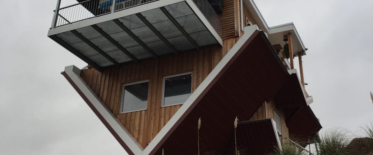 A modern, multi-level wooden house with a slanted roof and a balcony.