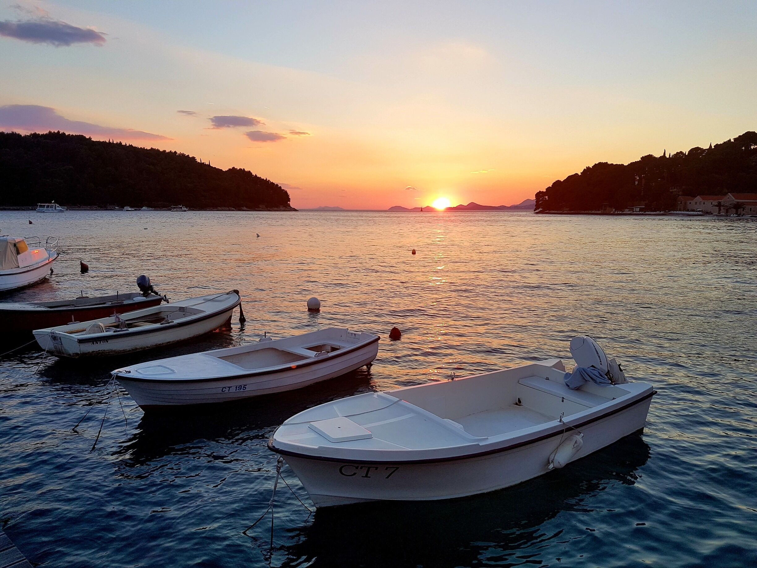 A sunset over a calm lake with several small boats anchored near the shore.