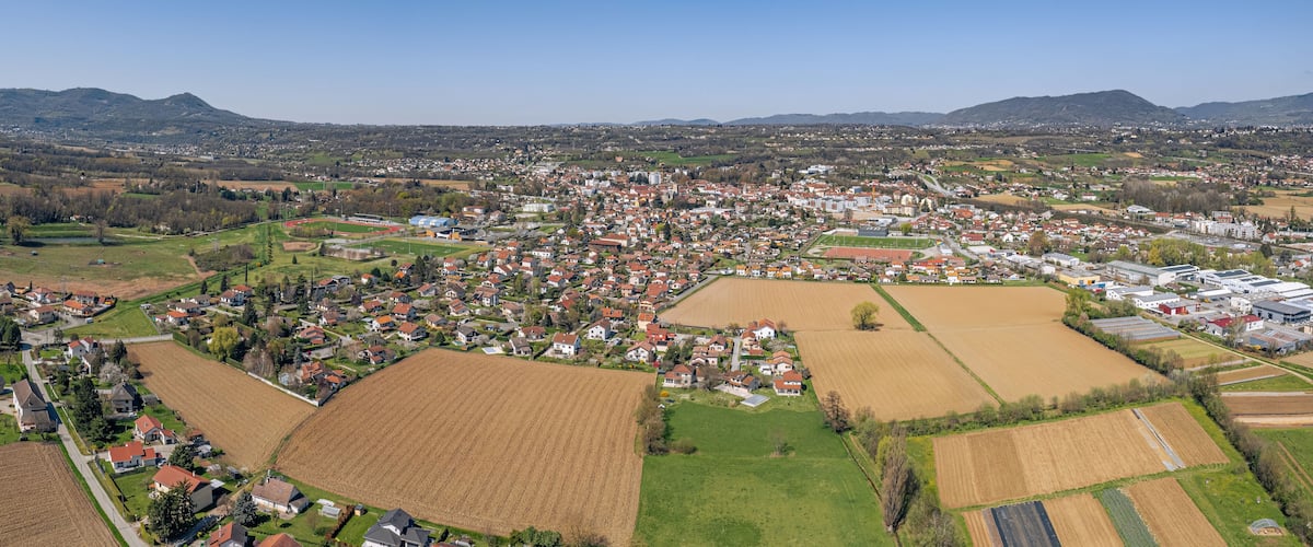 An aerial view of a town with residential areas, agricultural fields, and a mountainous backdrop.