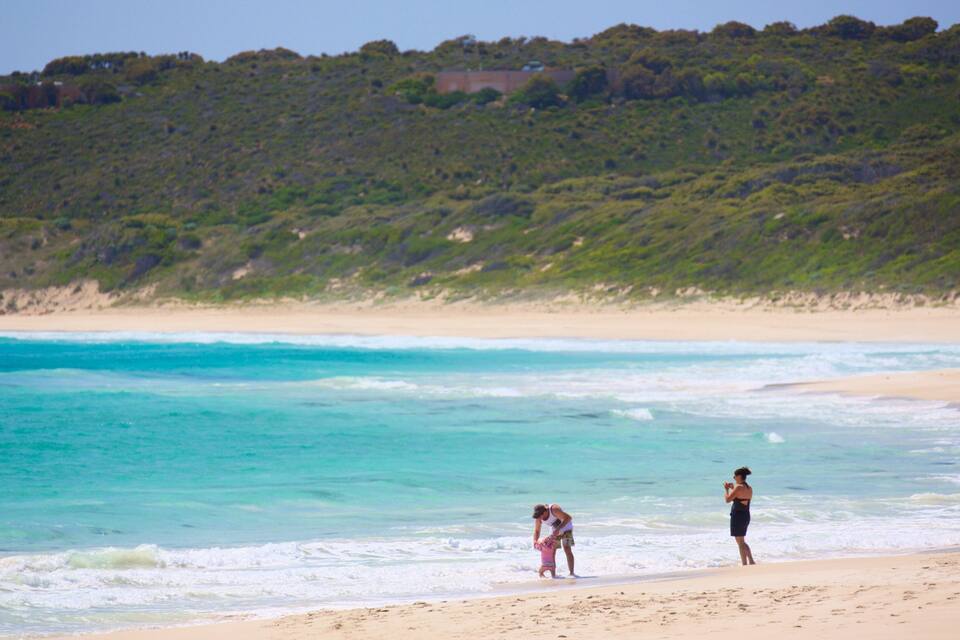 A beach with clear turquoise water, a sandy shore, and a hill with greenery in the background.
