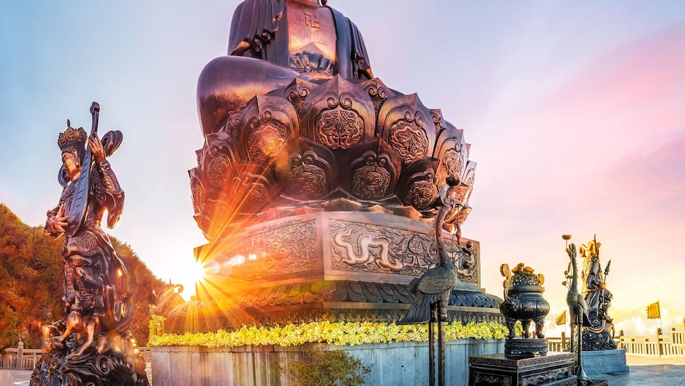 A large Buddha statue with intricate carvings, surrounded by smaller statues and traditional architecture.