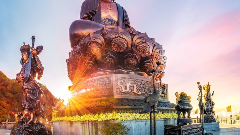 A large Buddha statue with intricate carvings, surrounded by smaller statues and traditional architecture.