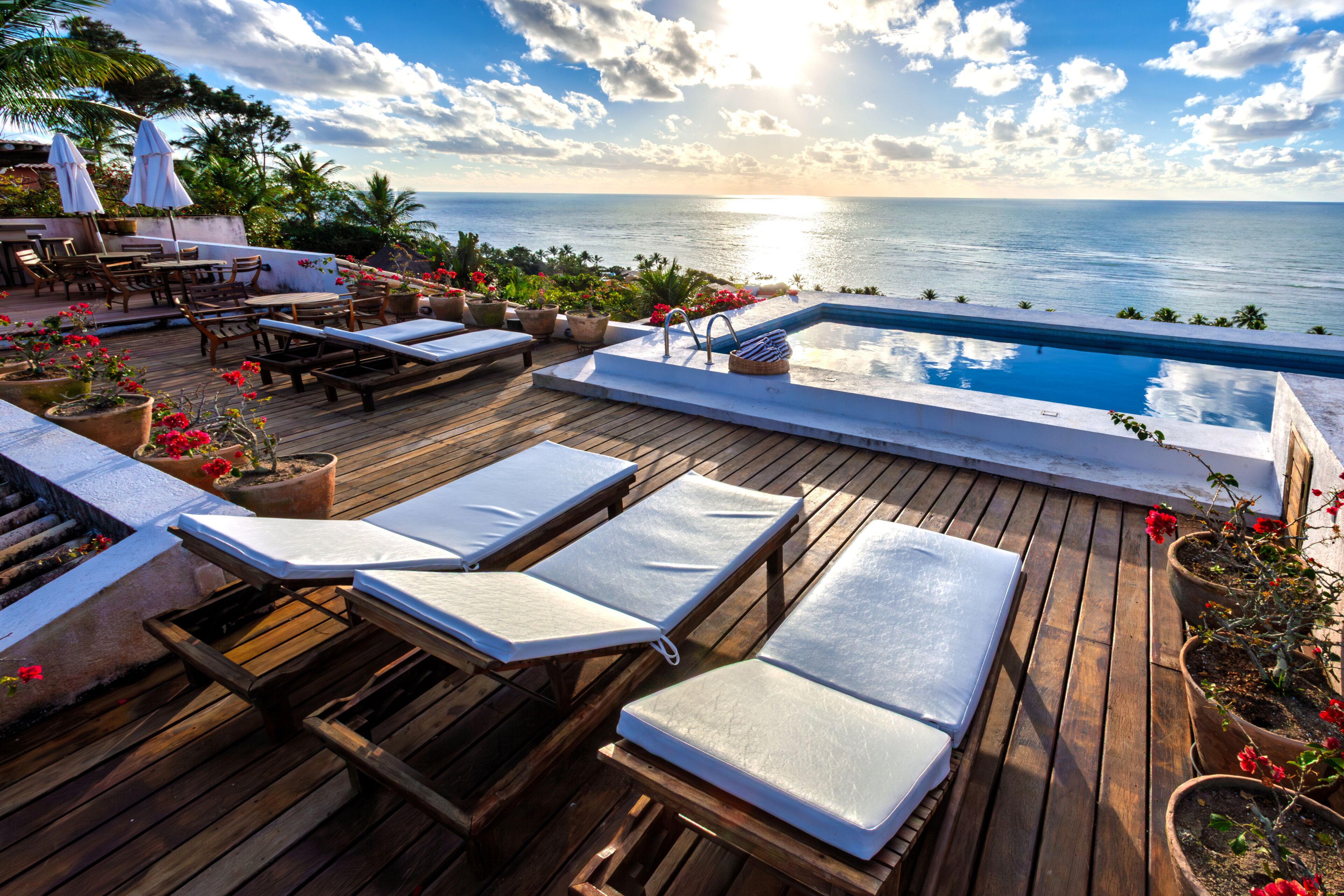 Um deck de madeira com cadeiras de descanso, uma piscina e vista para o oceano.