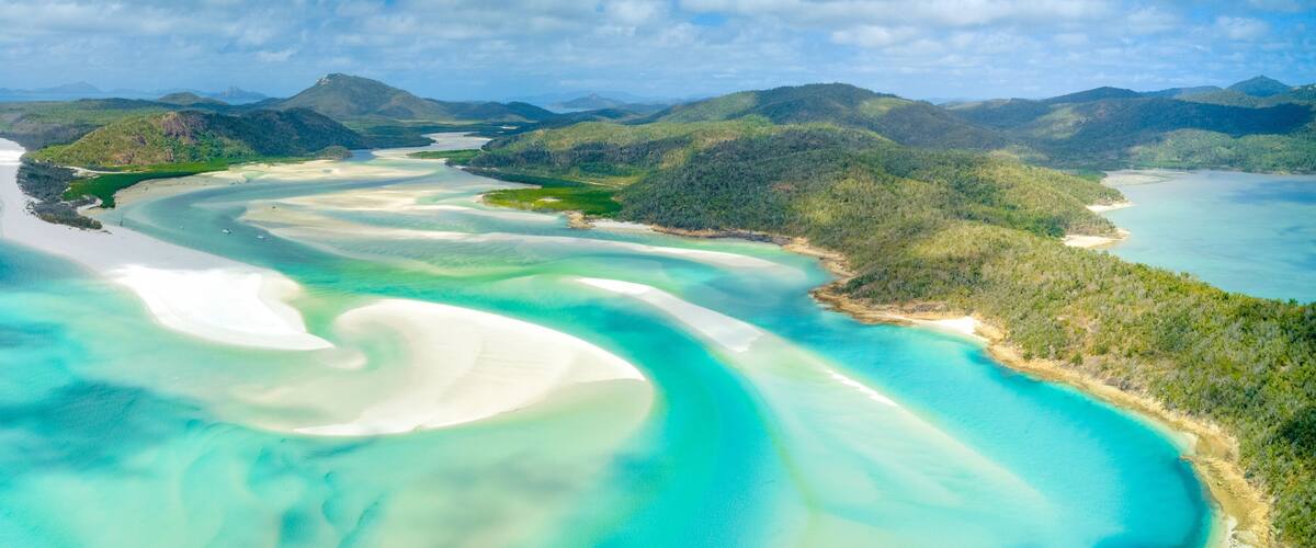 A coastal landscape with turquoise waters, white sand beaches, and green hills.