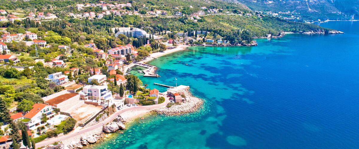 A coastal town with clear turquoise waters, a rocky shoreline, and mountainous terrain in the background.