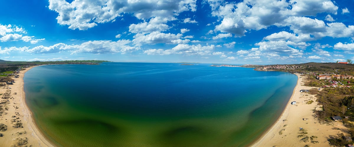 A coastal landscape with a large body of water, sandy beaches, and a small town with buildings.