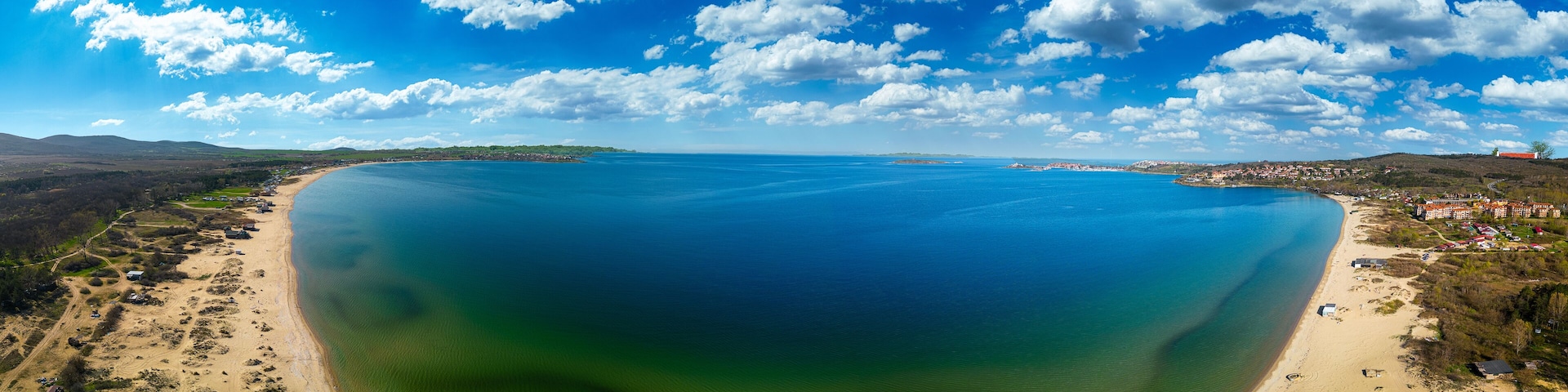 A coastal landscape with a large body of water, sandy beaches, and a small town with buildings.