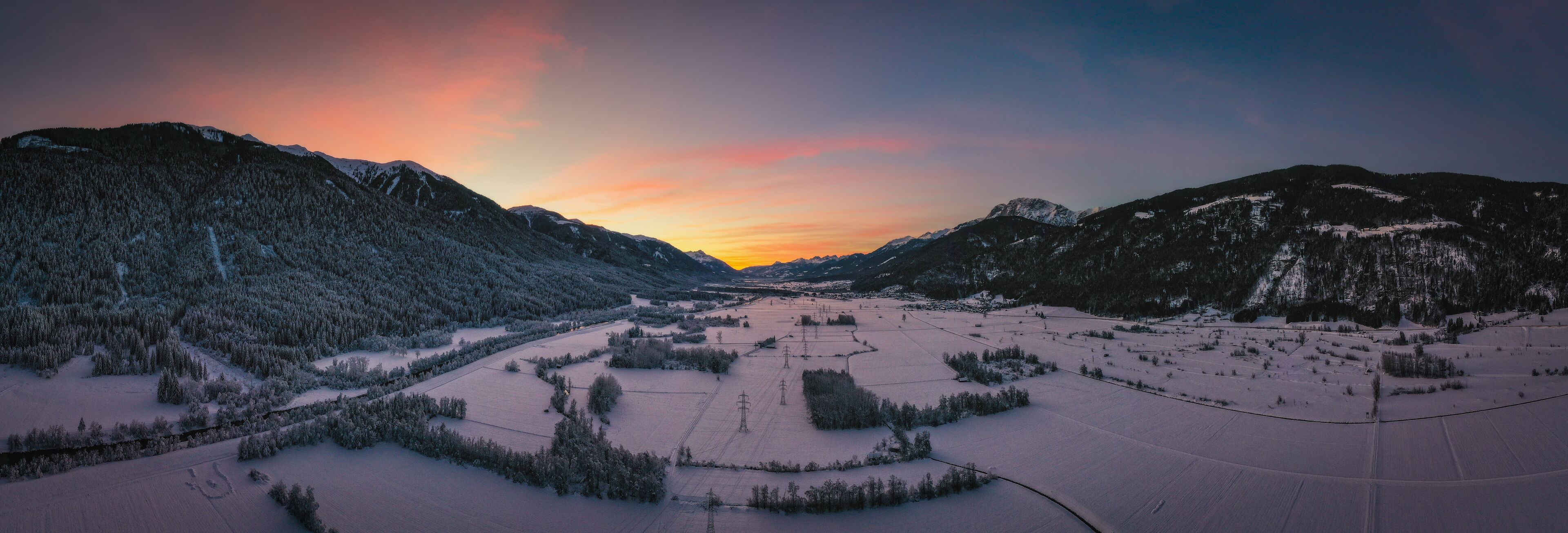 Un valle cubierto de nieve con montañas, un río y líneas eléctricas.