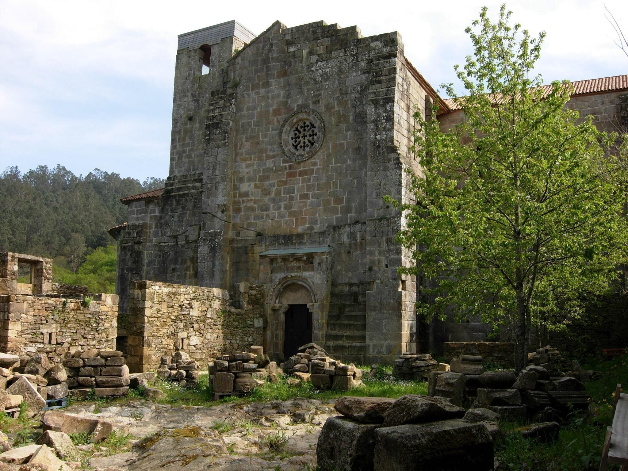 An ancient stone tower with a circular window and a doorway, surrounded by ruins and greenery.