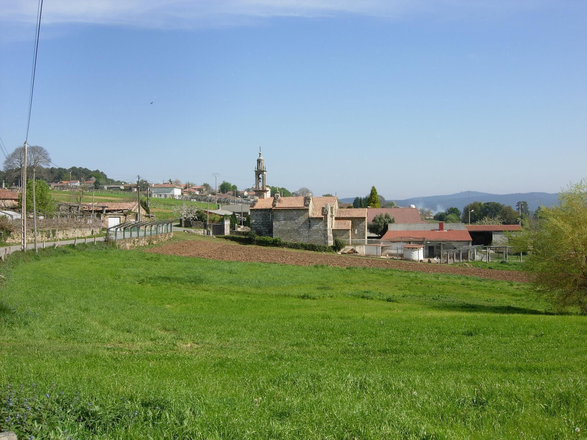 A rural landscape with a stone church, a bell tower, and a red-roofed building.