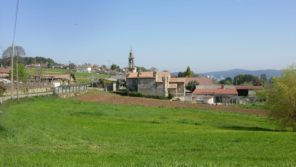 A rural landscape with a stone church, a bell tower, and a red-roofed building.