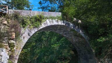 An old stone bridge over a river surrounded by lush greenery.